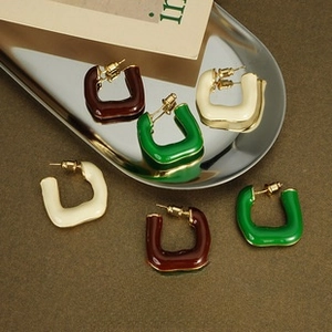 Detailed view of U-shaped enamel earrings in reddish-brown, dark green, and cream colors