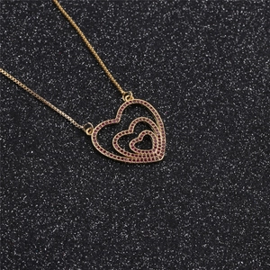 Macro detail of golden heart necklace featuring red zircon inlay on a textured background