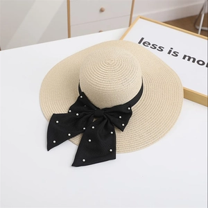 Detailed close-up of straw sun hat featuring a black ribbon bow with pearl accents