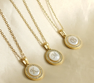 Détail de trois colliers initiaux dorés avec nacre blanche et accents de diamant