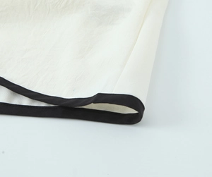 Close-up of white crepe fabric with black contrast trim and micro-wrinkle texture