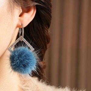Close-up of klein blue pompom earrings with geometric rhinstone studs on model