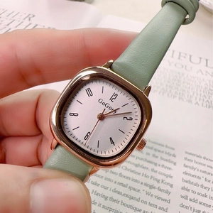 Close-up of square rose gold watch with green leather strap held against a book