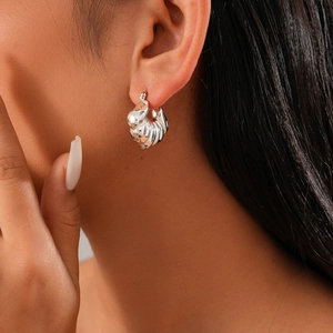 Macro detail of textured silver geometric shell hoop earring on model's ear