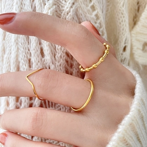 Close-up of gold wave and beaded rings worn on fingers against a warm knit background