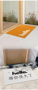 Detail view of PVC silk loop door mats in orange and beige with greeting text prints