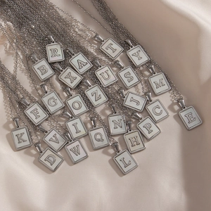 Flat lay of 26 alphabet pendants in silver with white shell inlay on cream velvet fabric