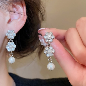 Detailed view of silver flower earrings with clear rhinestones and hanging white pearls