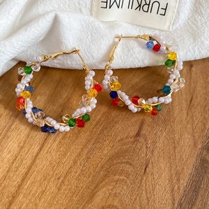 Detailed close-up of handmade crystal and pearl beaded hoop earrings on white fabric