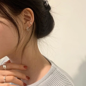Detail shot of silver twisted hoop earrings and stackable rings worn by a model