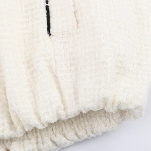 Detailaufnahme der cremeweißen Tweed-Stoffstruktur und des Rippsaums einer Freizeitjacke