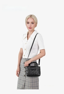 Quilted black handbag with square stitching and top handle shown on fashion model