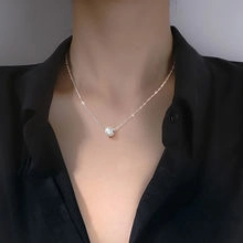 Close-up of a silver necklace with a white pearl pendant on a model wearing black