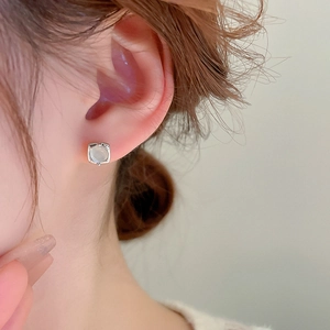 Close-up of a minimalist silver square stud earring with a white cat eye stone inlay