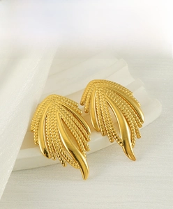 Detail of 18K gold-plated braided leaf earrings on a minimalist white backdrop