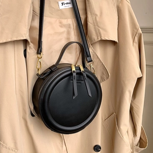 Retro black round leather handbag with gold zipper and detachable strap on beige coat