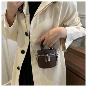 Détail d'un mini sac cylindrique en cuir PU marron avec surpiqûres et chaîne argentée