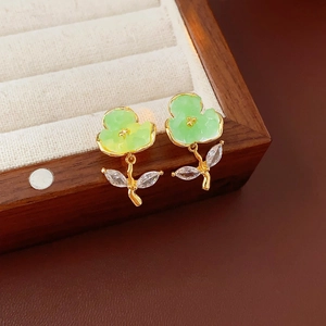 Close-up of green crystal flower earrings with gold plating on a wooden jewelry box