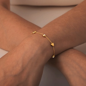 Detail of a gold flat cross chain bracelet featuring heart charms and white gemstones