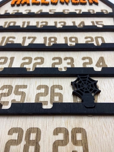 Detail of wooden Halloween countdown calendar showing engraved dates and spider web marker