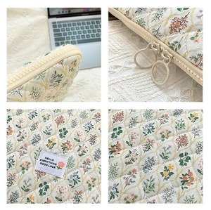 Detail view of floral quilted laptop sleeve with beige double zippers and woven label