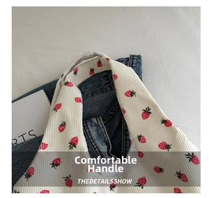 Detail of the white corduroy tote bag showing red strawberry prints and sturdy handles