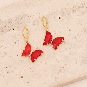Elegant 18K gold butterfly earrings with red gemstones on a beige stone background
