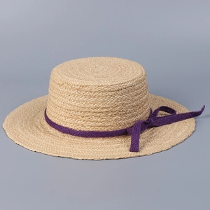 Detail of raffia boater hat with a purple ribbon bow showing fine straw weave texture