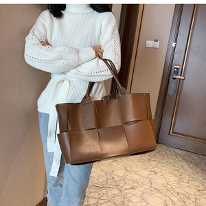 Detailed view of a brown woven leather tote bag held by a model in a casual outfit