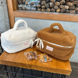 Detail of plush lamb wool makeup bags in white and brown with ribbon zippers and woven labels