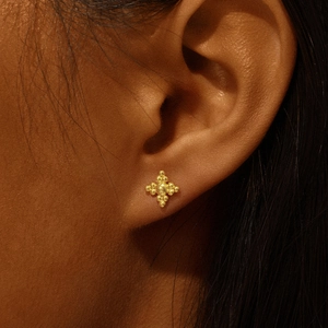 Macro shot of a golden cross-shaped stud earring with bead details worn on the earlobe