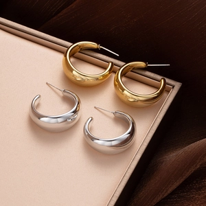 Polished gold and silver thick C-shape hoop earrings displayed on silk texture