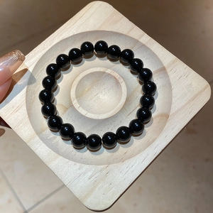 Macro detail of polished black obsidian beaded bracelet on a square wooden display tray