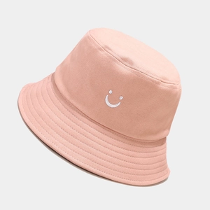 Close-up of pink cotton bucket hat featuring white smiley face embroidery and stitched brim