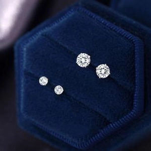 Macro shot of silver round claw-set stud earrings in a blue velvet jewelry box
