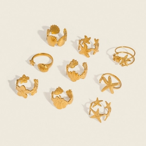 Golden stainless steel ocean ring set with starfish and seashell charms on plain surface