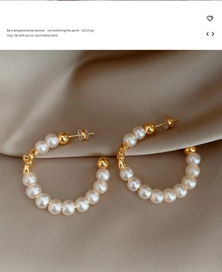 Detail of C-shaped pearl hoop earrings with gold metal beads on champagne satin
