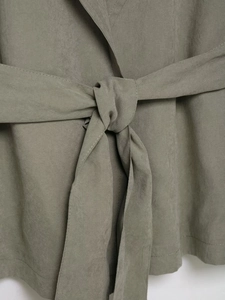 Detailed view of the belted waist with knot and suede texture on a sage green trench coat