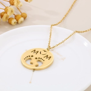 Close-up of golden MOM pendant with baby footprints on a white ceramic tray