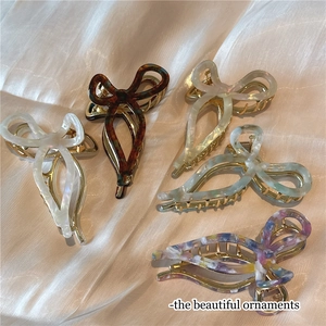 Five acetate bow hair clips in amber and pearl finishes on silk background