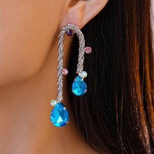 Detail of silver twisted metal drop earrings featuring large blue crystals and rhinestones