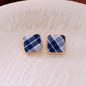 Détail de boucles d'oreilles dorées carrées avec tissu à carreaux bleu et blanc