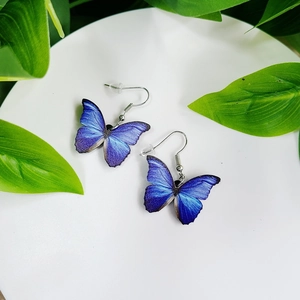 Macro detail of vivid blue butterfly wing earrings on a minimalist white ceramic tray