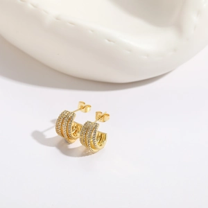 Macro detail of gold C-shaped earrings featuring four rows of sparkling white zircon stones