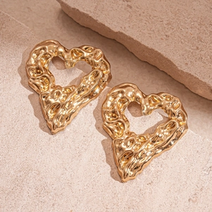 Vintage golden hollow heart earrings with molten metal texture on natural stone background