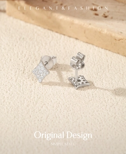 Macro shot of silver diamond-set rhombus stud earrings on a natural stone background