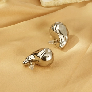 Gros plan de boucles d'oreilles gouttes de lave argentées sur fond de soie jaune