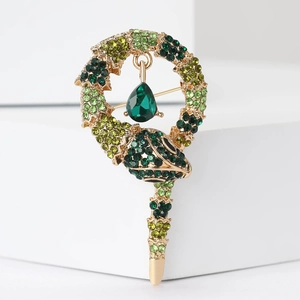 Detail of gold snake brooch with green crystals and teardrop pendant on white base