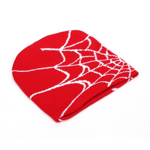 Detail of red knitted beanie featuring a white spider web jacquard pattern on soft fabric