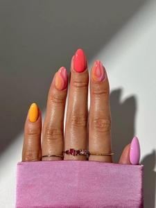 Macro detail of almond-shaped press-on nails in pink, yellow, and wavy orange patterns